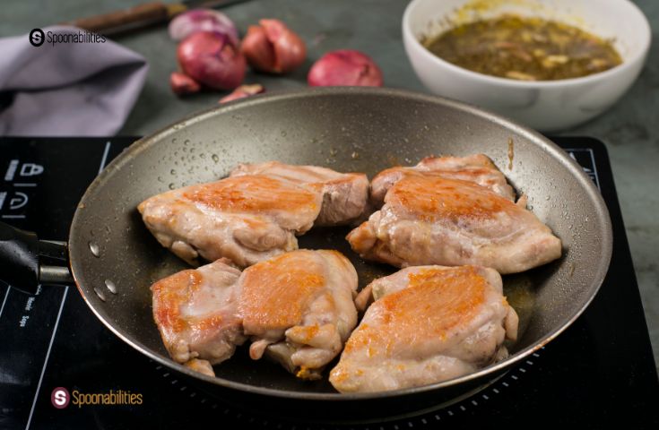 A photo of four chicken thighs browning in a pan.