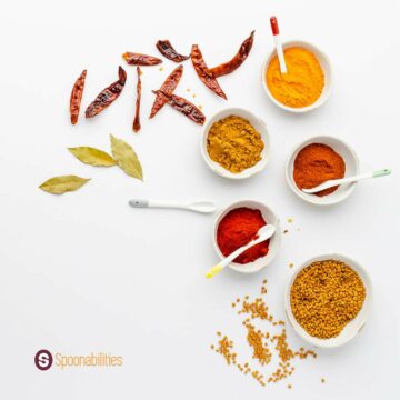 a photo of Spices and Salts in small white bowls with bay leaves and dried chili on the side