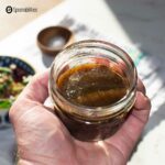 A photo of a hand holding a small jar with a mixture of traditional vinaigrette ingredients