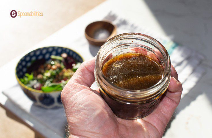 A photo of a hand holding a small jar with a mixture of traditional vinaigrette ingredients