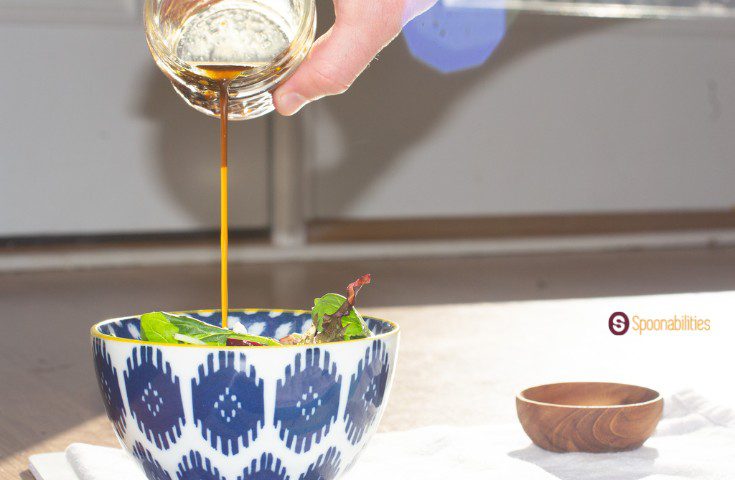 A photo of a hand holding a jar drizzling the traditional vinaigrette in a bowl of salad