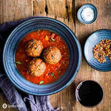 Three meatballs in a blue bowl with two small saucers with condiments on the left side.