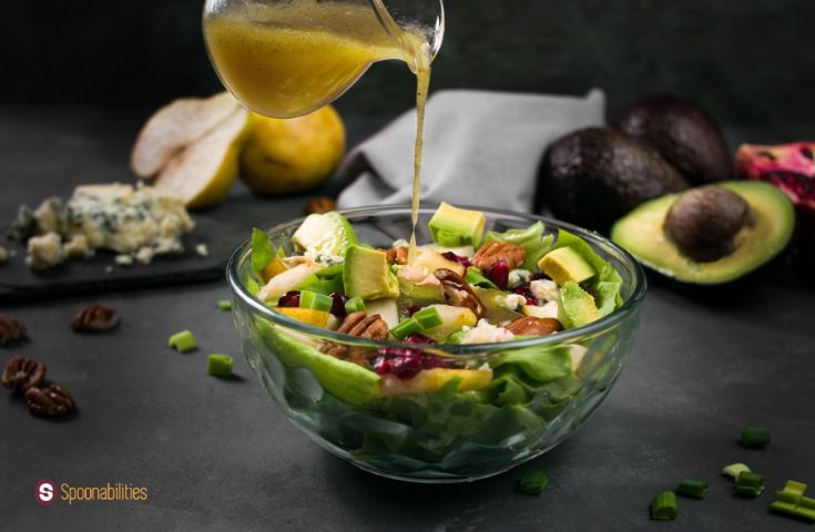 a photo pouring Honey mustard vinaigrette on butter lettuce pear salad in a clear bowl