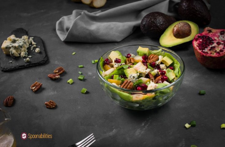 Honey mustard vinaigrette on butter lettuce pear salad in a clear bowl with some of the ingredients on the side, fork, and a gray cloth