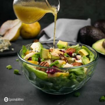 pouring Honey mustard vinaigrette on butter lettuce pear salad in a clear bowl