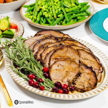 The lamb is plated in an oval plate and garnished with fresh rosemary and cranberries.