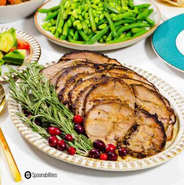 The lamb is plated in an oval plate and garnished with fresh rosemary and cranberries.