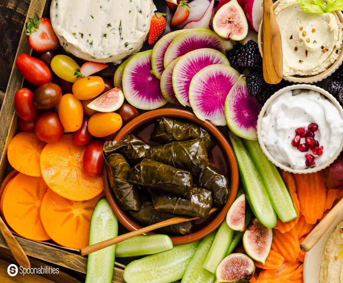 Vegan charcuterie tray with fresh veggies and fruits, dolmas, tzatziki, vegan cheese