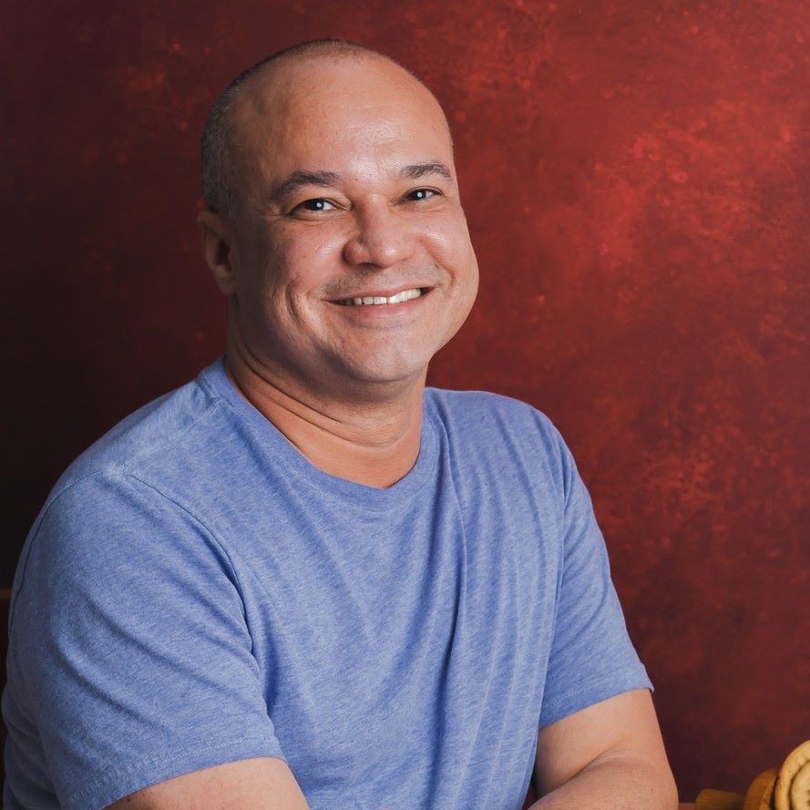 Carlos Leo, photographer, smiling in a blue shirt with a red background