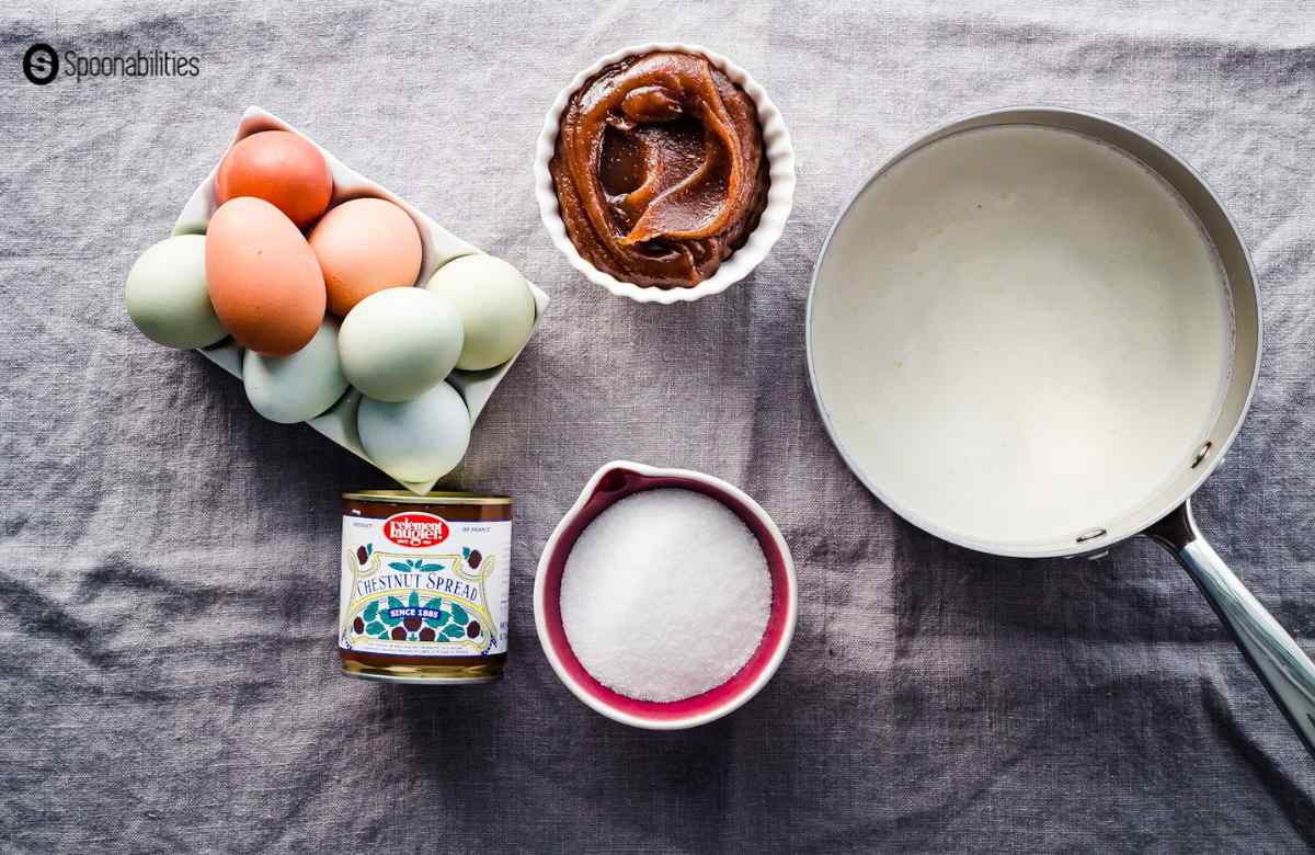 Prepared ingredients for chestnut creme brulee consisting of eggs, milk in a saucepan, chestnut spread in a saucer and sugar