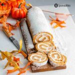Slices of Pumpkin Roll with cream cheese filling on a wooden board with fall theme decor all around