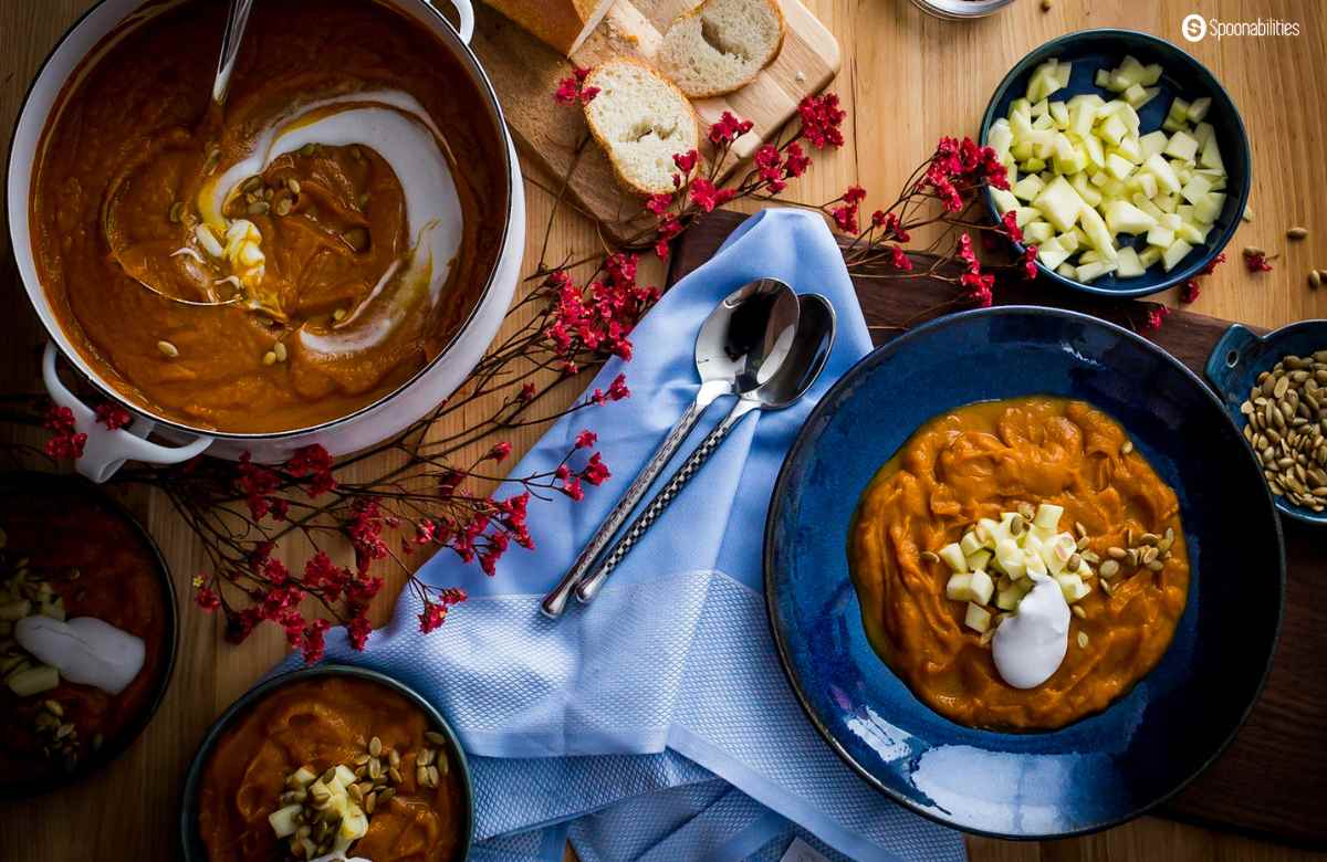 Roasted pumpkin bisque in bowls and in its pot arranged beautifully on the table with bread and toppings