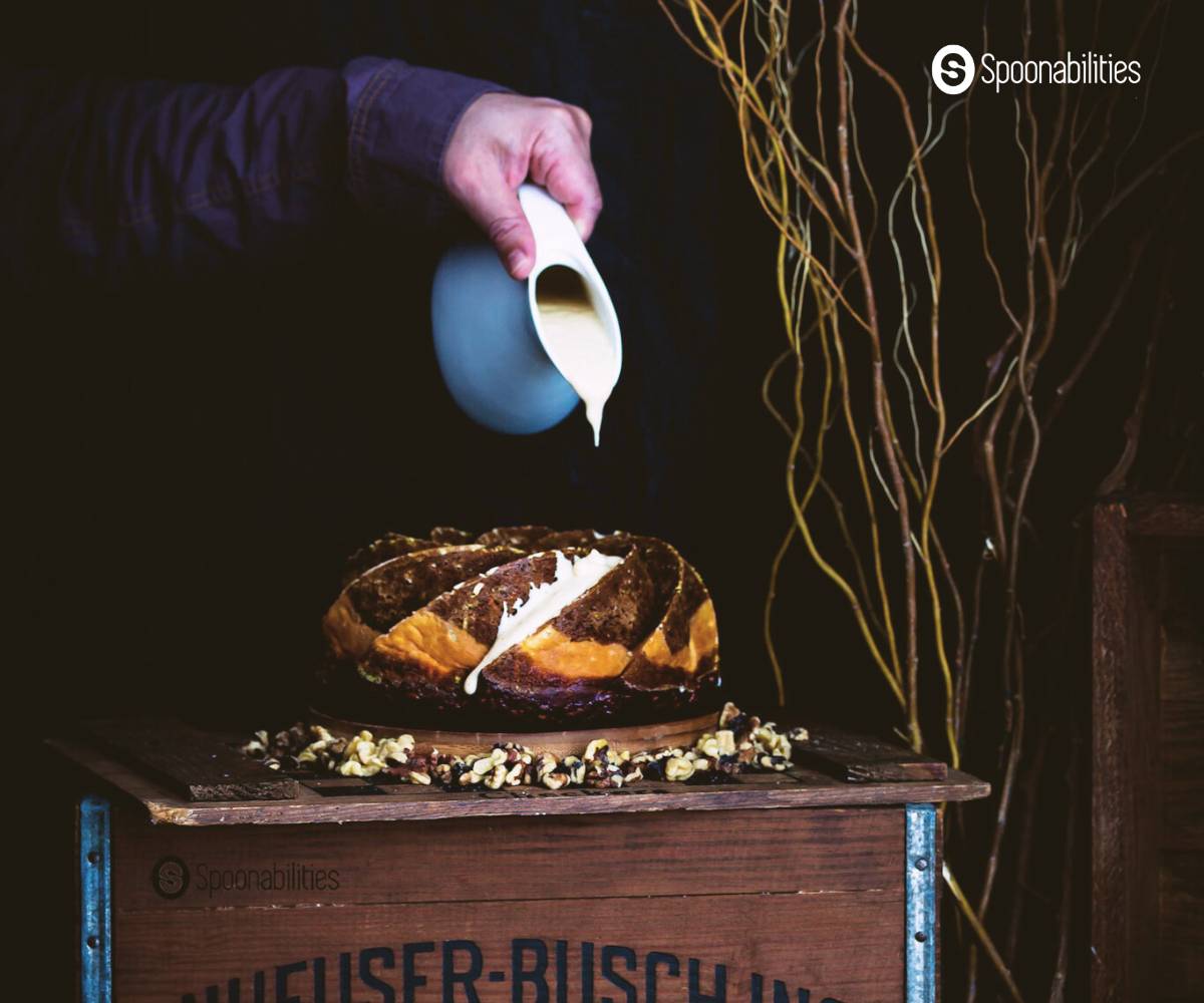 Pouring cream cheese sauce from a blue jug on the carrot pumpkin bundt cake