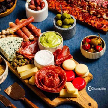 Rectangular wooden charcuterie board with meats and cheese and olives on small bowls next to it