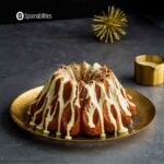 Brandy eggnog bundt cake in a gold plate with drizzle container at the side