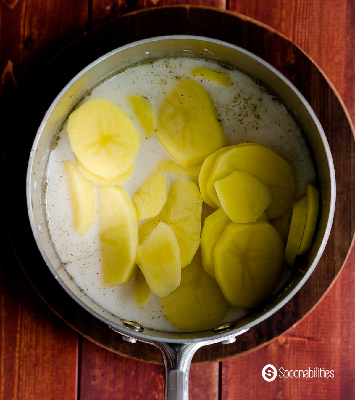 Sliced potatoes for gratin soaked in milk in a pot
