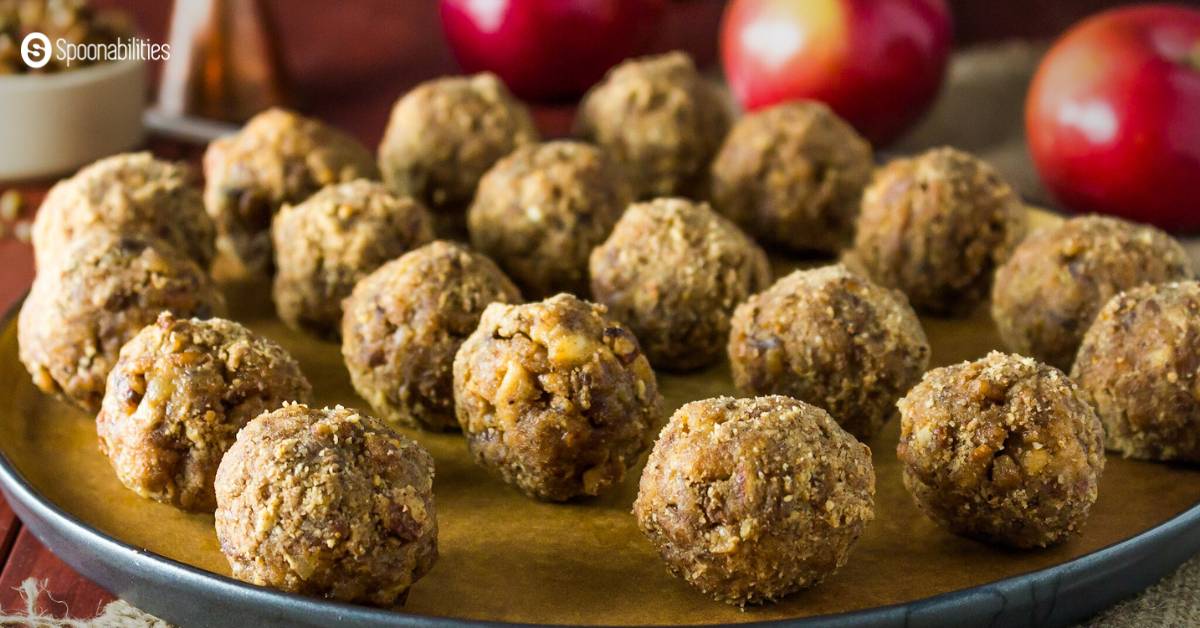 Several mini caramel apples arranged in a plate with red apples in the background