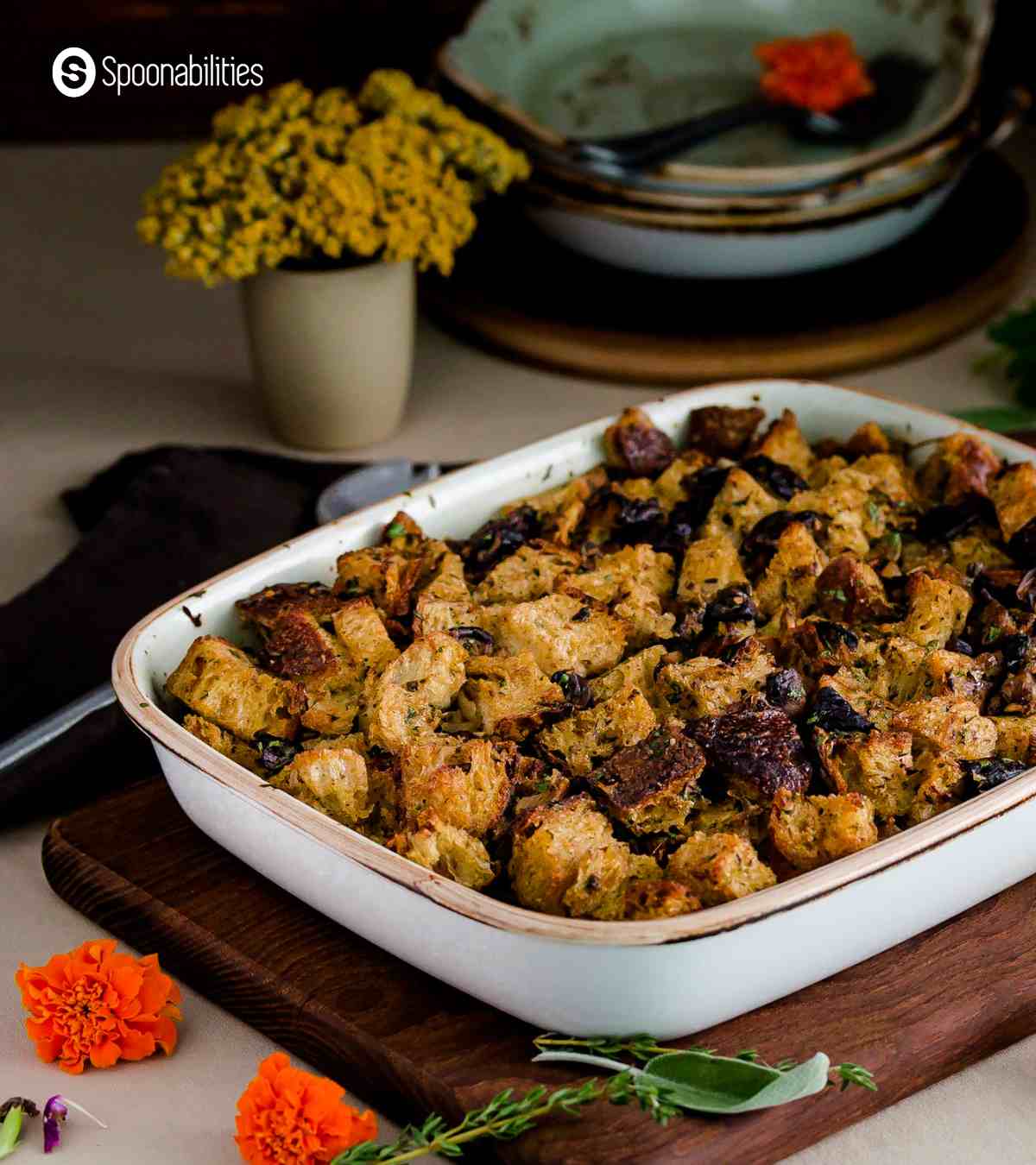 Mushroom stuffing in a baking dish with orange flowers in the foreground and yellow flowers in a pot at the background