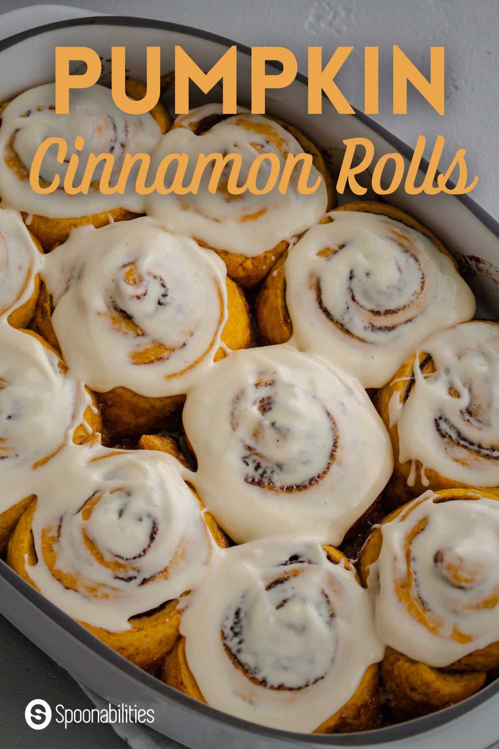 close up of pumpkin cinnamon rolls with glaze in large white baking dish