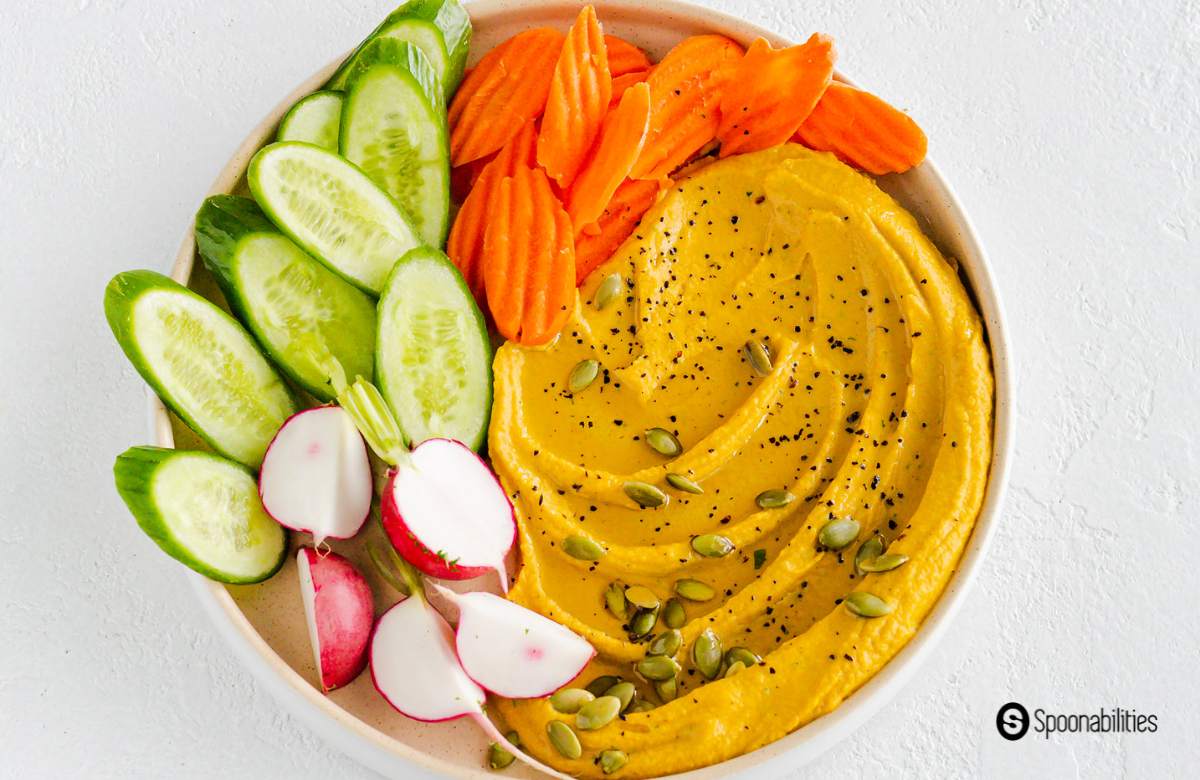 Pumpkin hummus dip on an appetizer plate with fresh sliced cucumbers carrots and radish