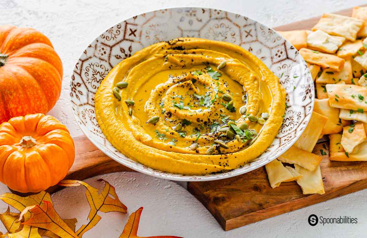 pumpkin hummus with pita chips on the side and a couple of pumpkin decorations