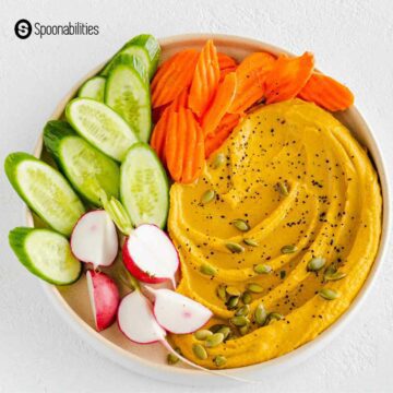 Pumpkin hummus with pumpkin seeds on top in an appetizer plate with sliced fresh vegetables