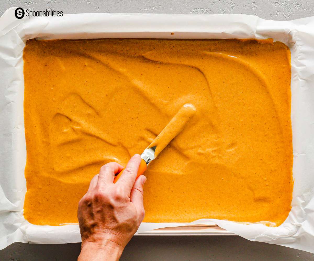 Spreading the pumpkin cake mixture using a spatula on a baking sheet lined with parchment paper