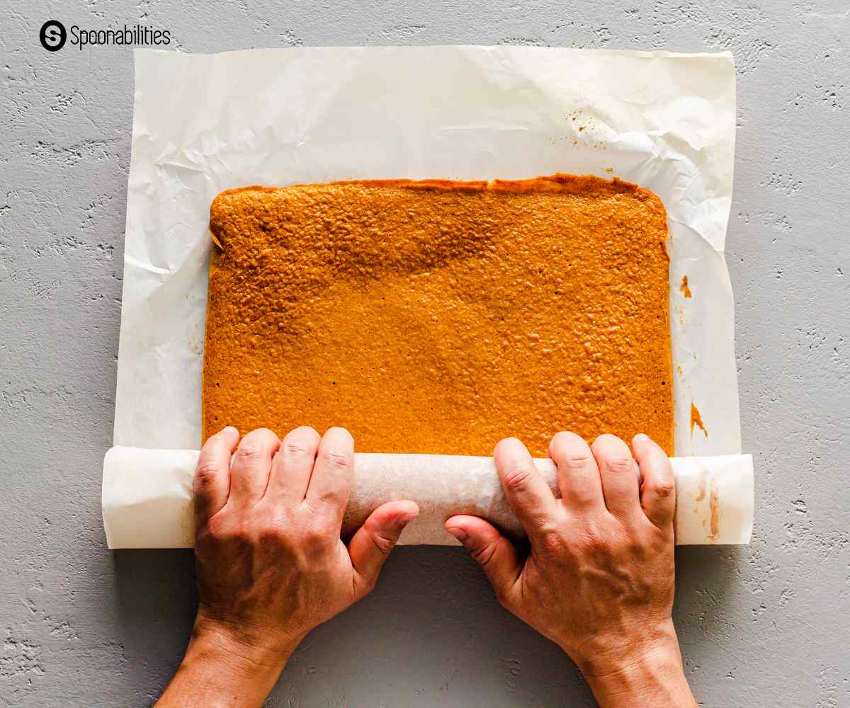 Rolling the pumpkin cake on a parchment paper