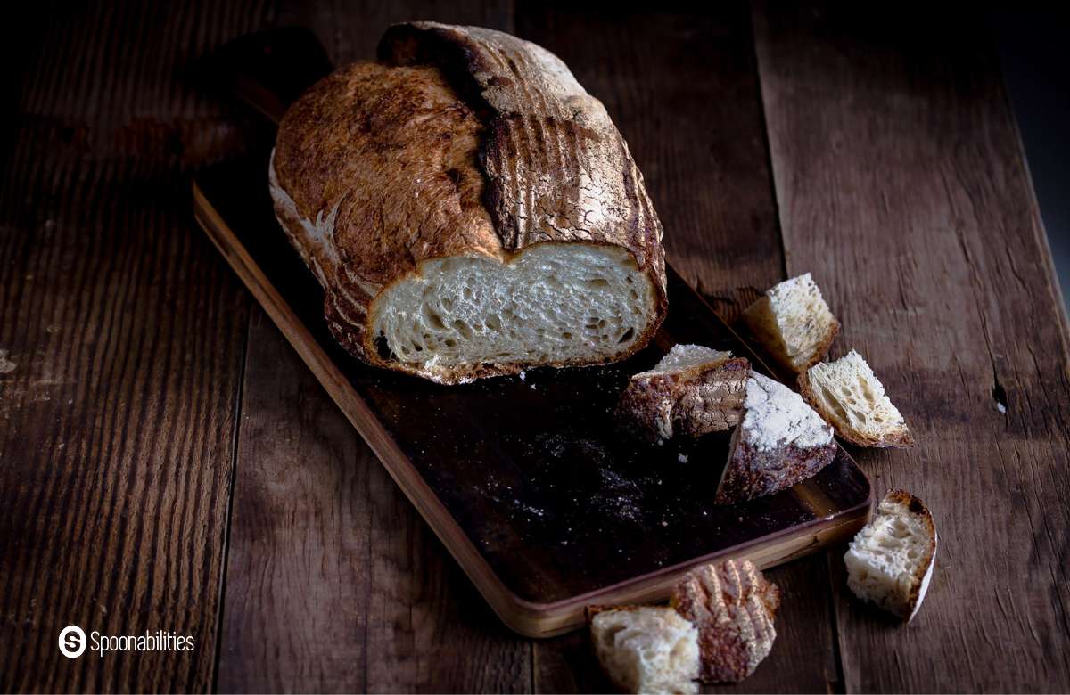 Sourdough bread loaf on a wooden chopping board with a bunch of bread chopped scattered around