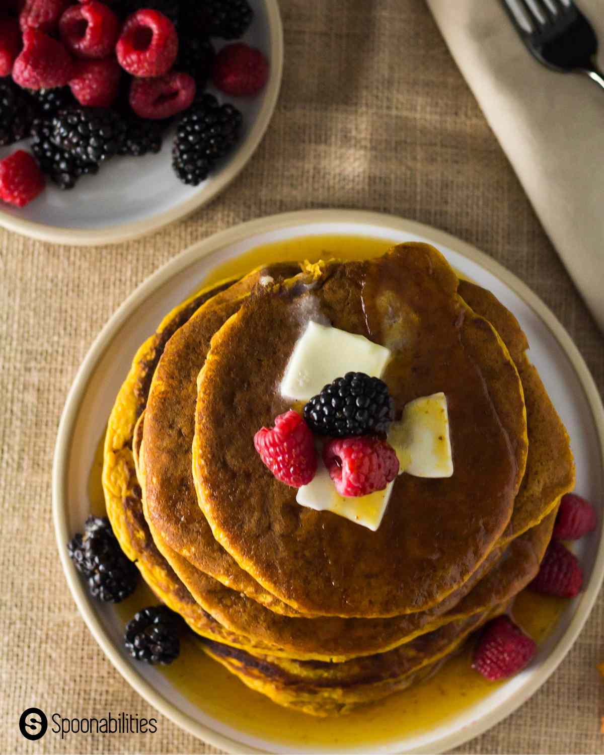 Top view of a plate of pumpkin spice pancakes with butter, mixed berry toppings and maple syrup