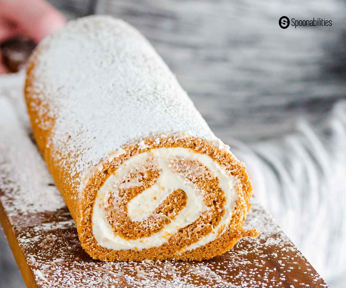 pumpkin roll with cream cheese filling and powdered sugar dusting on a wooden board