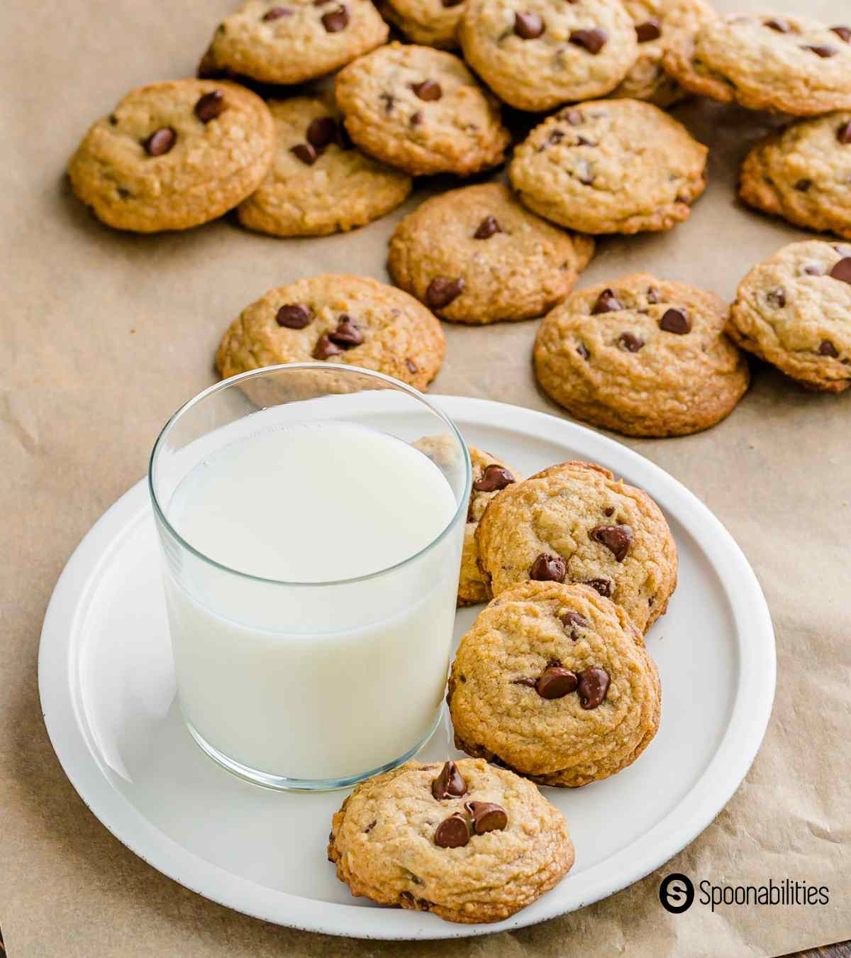 Chocolate chip cookies on a plate with milk and more cookies in the background