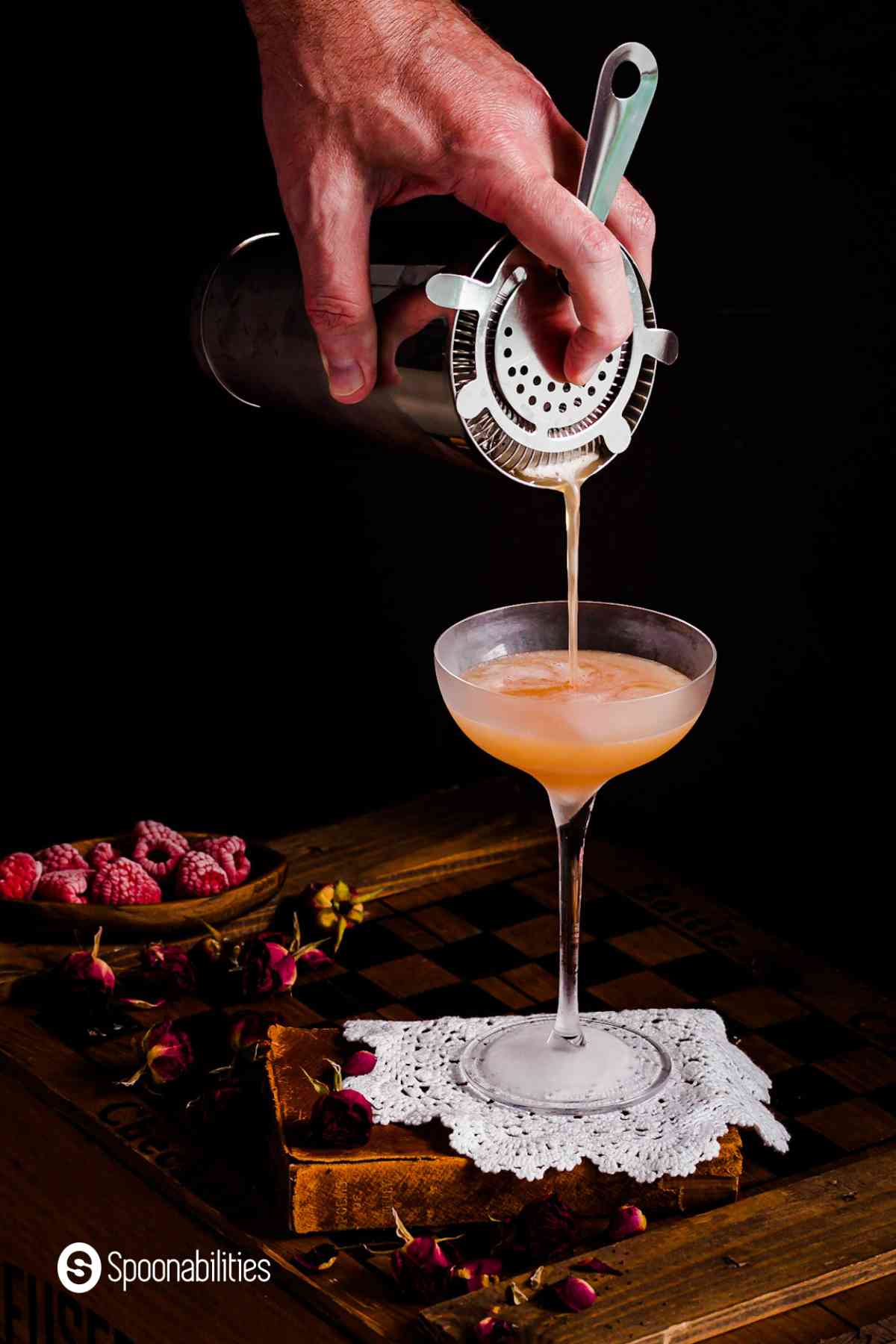 Hand pouring drink from a shaker with strainer into a chilled cocktail glass