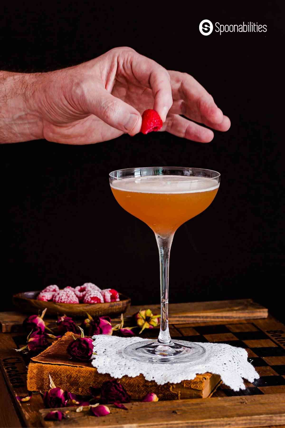 Hand placing a frozen raspberry on top of french martini in a cocktail glass