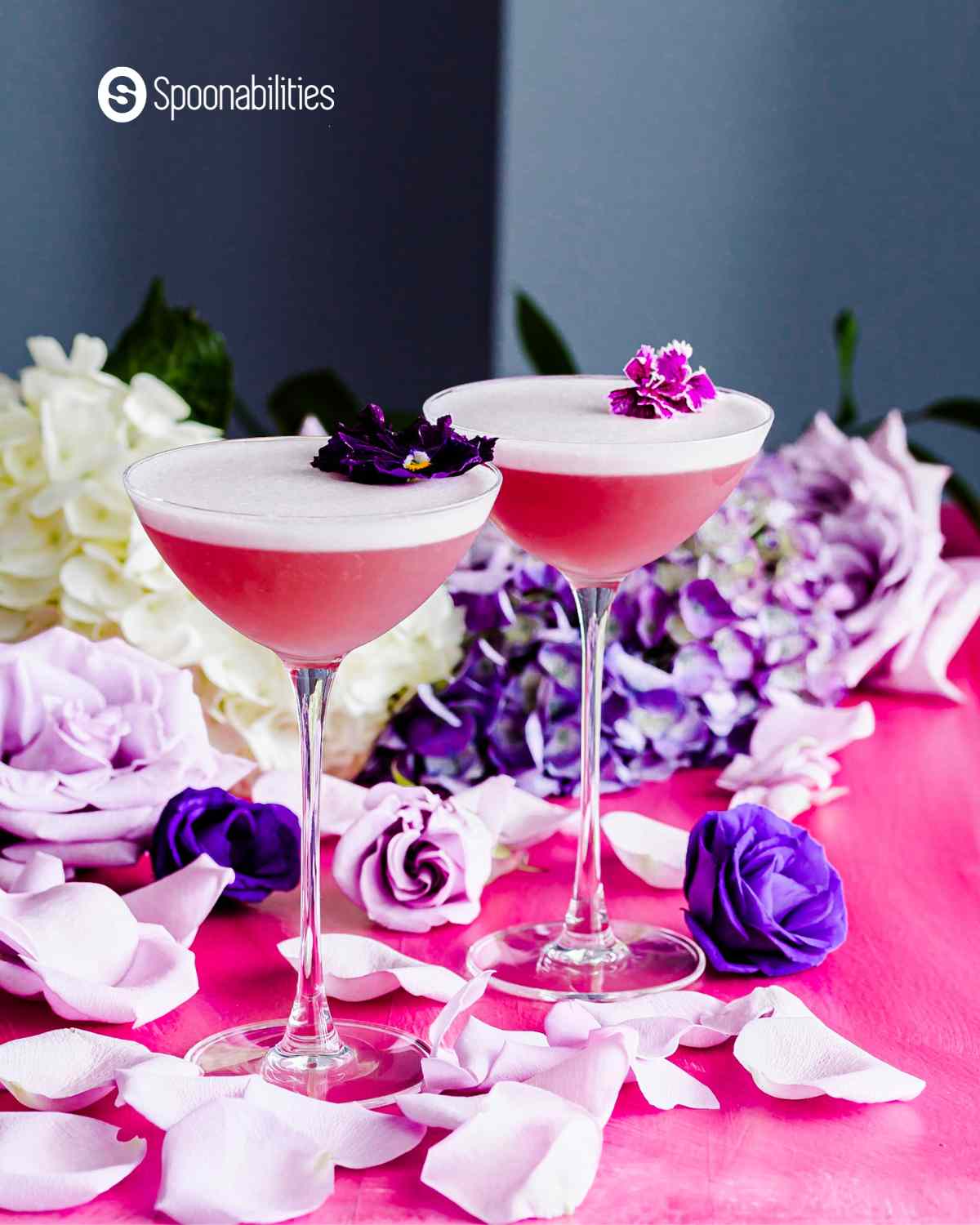 gin violette cocktails with flowers in the background and flower petals in the foreground