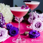 A tall gin violette cocktail in focus