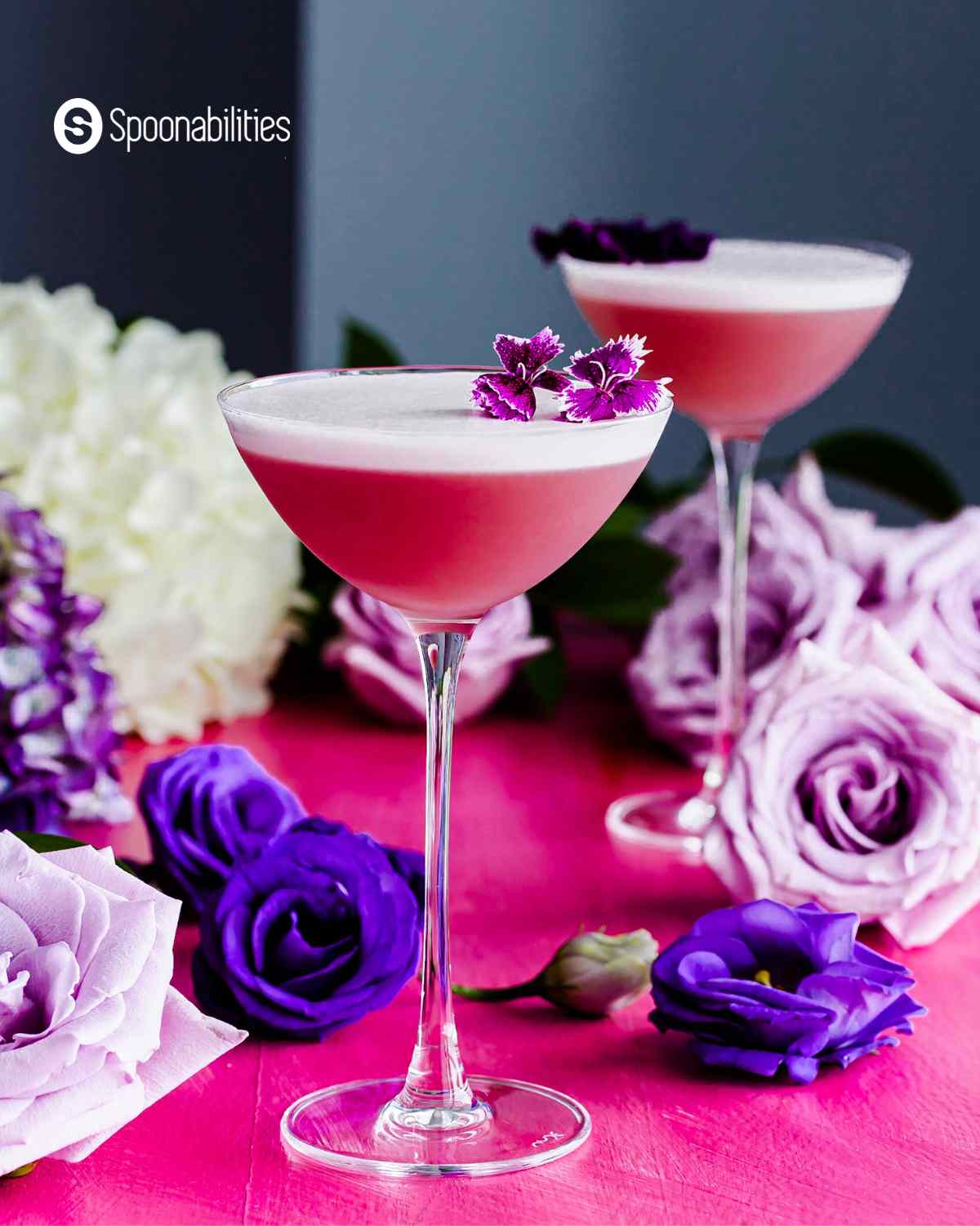 gin violette cocktail in a clear glass with violet and purple colored flowers in the background