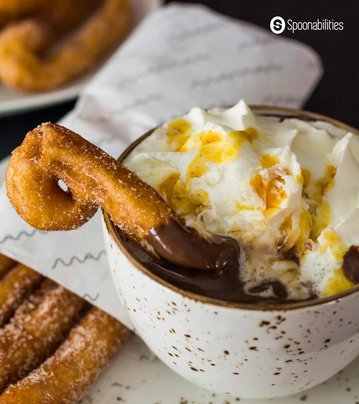 Sugary churros dipped in a cup of thick hot chocolate with cream on top