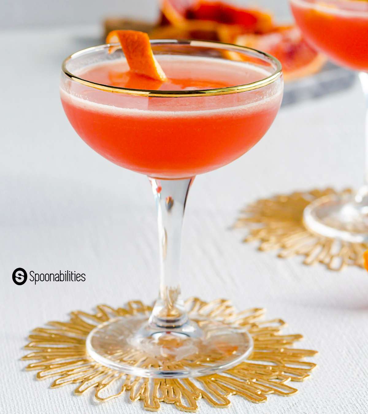 Solerno cocktail in a glass with gold trimming in the rim and orange zest as garnish