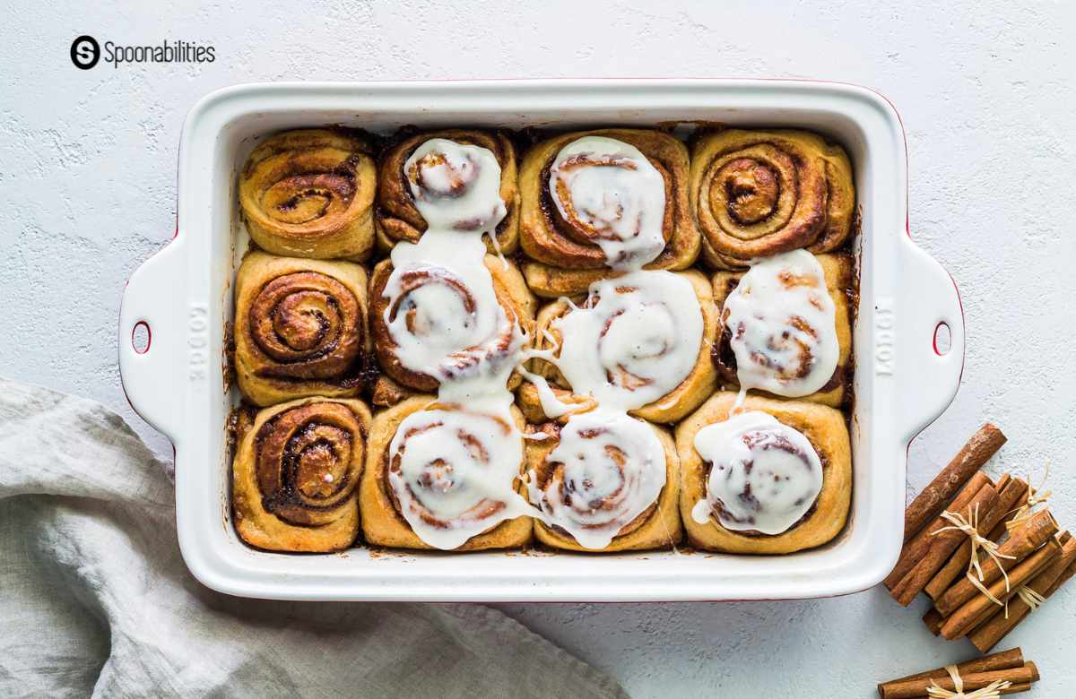 A dozen cinnamon rolls with frosting in a whit baking dish