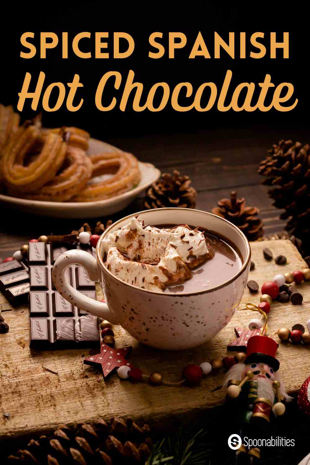 A cup of Spanish hot chocolate with churros in the background among chocolate bars and chips and Christmas holiday ornaments