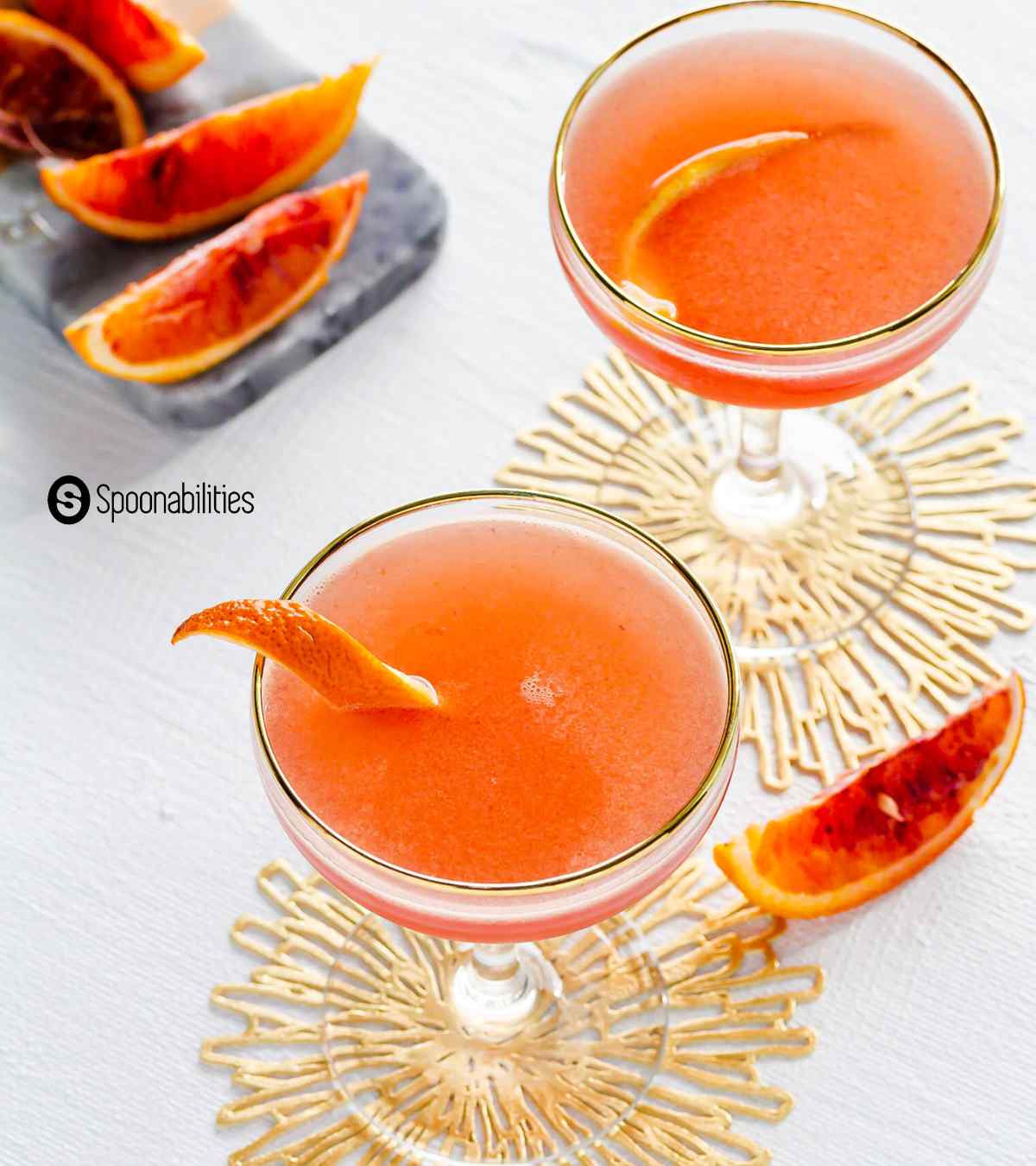 A couple of blood orange solerno cocktails with blood orange wedges in the background